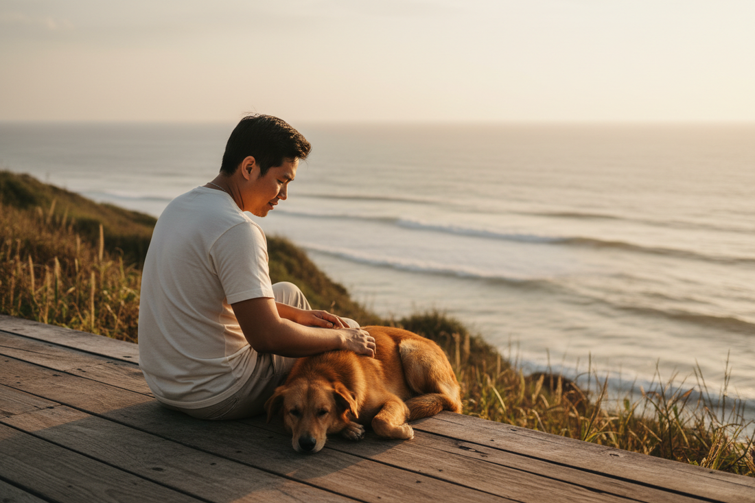 Man sitting beside his dog near the ocean, representing the bond between a pet guardian and companion.