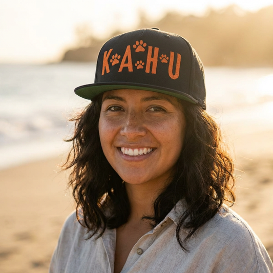 Person wearing a black cap with 'KAHU' text and paw print graphic design - Island Drops hat collection | Unisex snapback caps