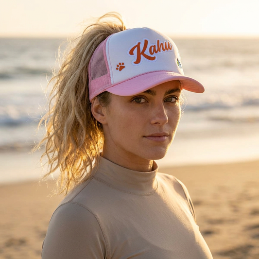 Woman wearing a pink and white cap with 'Kaha' branding on a beach  - Island Drops hat collection | Unisex cap